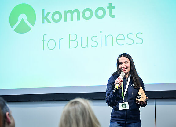 2025_komoot-Partner-Awards-2024-Vergabe-Rede_Gabriele-Giessenboeck Frau redet in Mikrofon mit komoot Partner Award 2024 in der Hand
