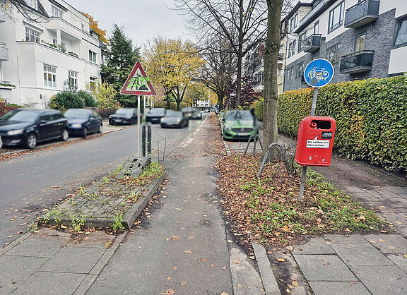 Die Klaerchenstraße: Parkende Kfz auf beiden Seiten, breite Fahrspur für Kfz, dafür kaum Platz für Fuß- und Radverkehr.