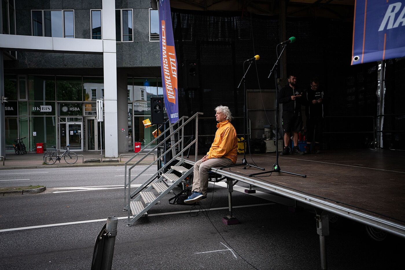 Mann im orangenen Hoodie sitzt auf der Bühne vor einem leeren Platz