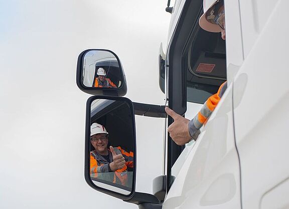 Lkw-Fahrer guckt in den linken Außenspiegel und hebt den Daumen