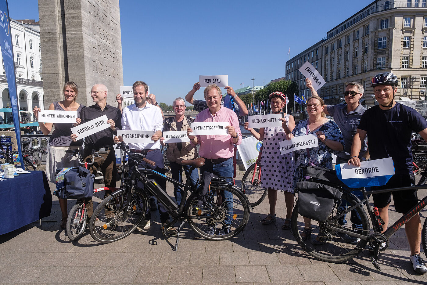 Eine Gruppe Menschen zur Eröffnung des STADTRADELN. Sie halten Schilder ins Bild mit Gründen warum sie beim STADTRADELN dabei sind.