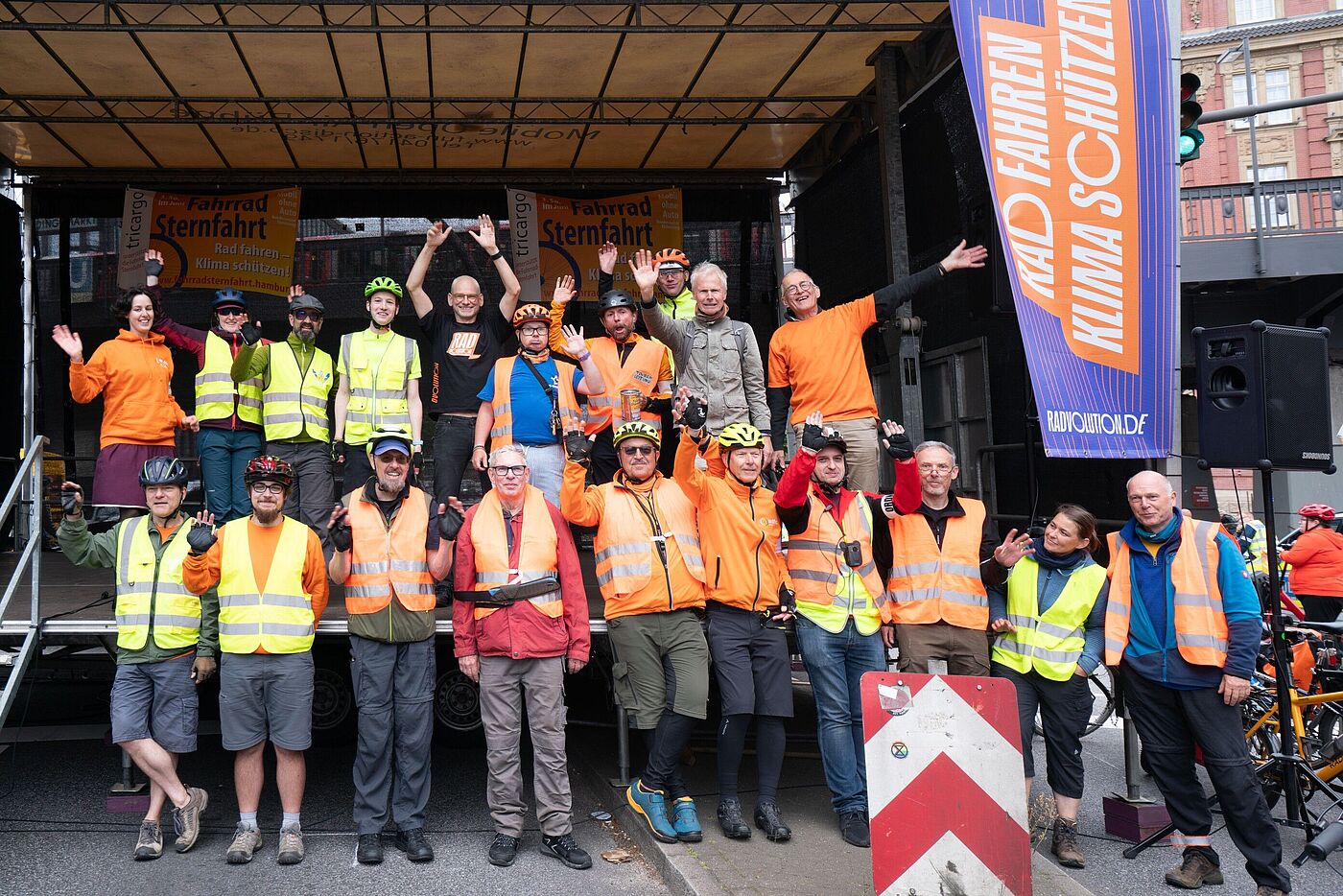 Gruppe von Radfahrenden vor einer Bühne, winkend