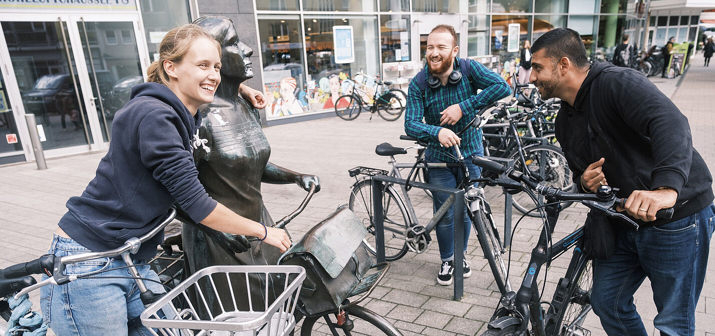 STADTRADELN_2022_Ergebnisse Drei junge Leute fröhlich mit Fahrrädern an einer Radfahrerinnen-Statue
