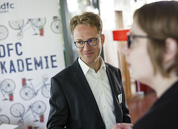 Ein junger Mann mit Brille lächelt, Im HIntergrund ADFC-Akademie-Werbung