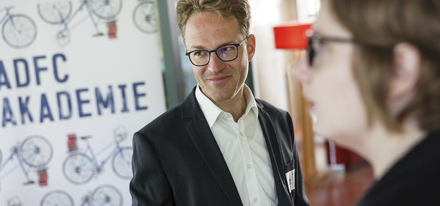 Ein junger Mann mit Brille lächelt, Im HIntergrund ADFC-Akademie-Werbung