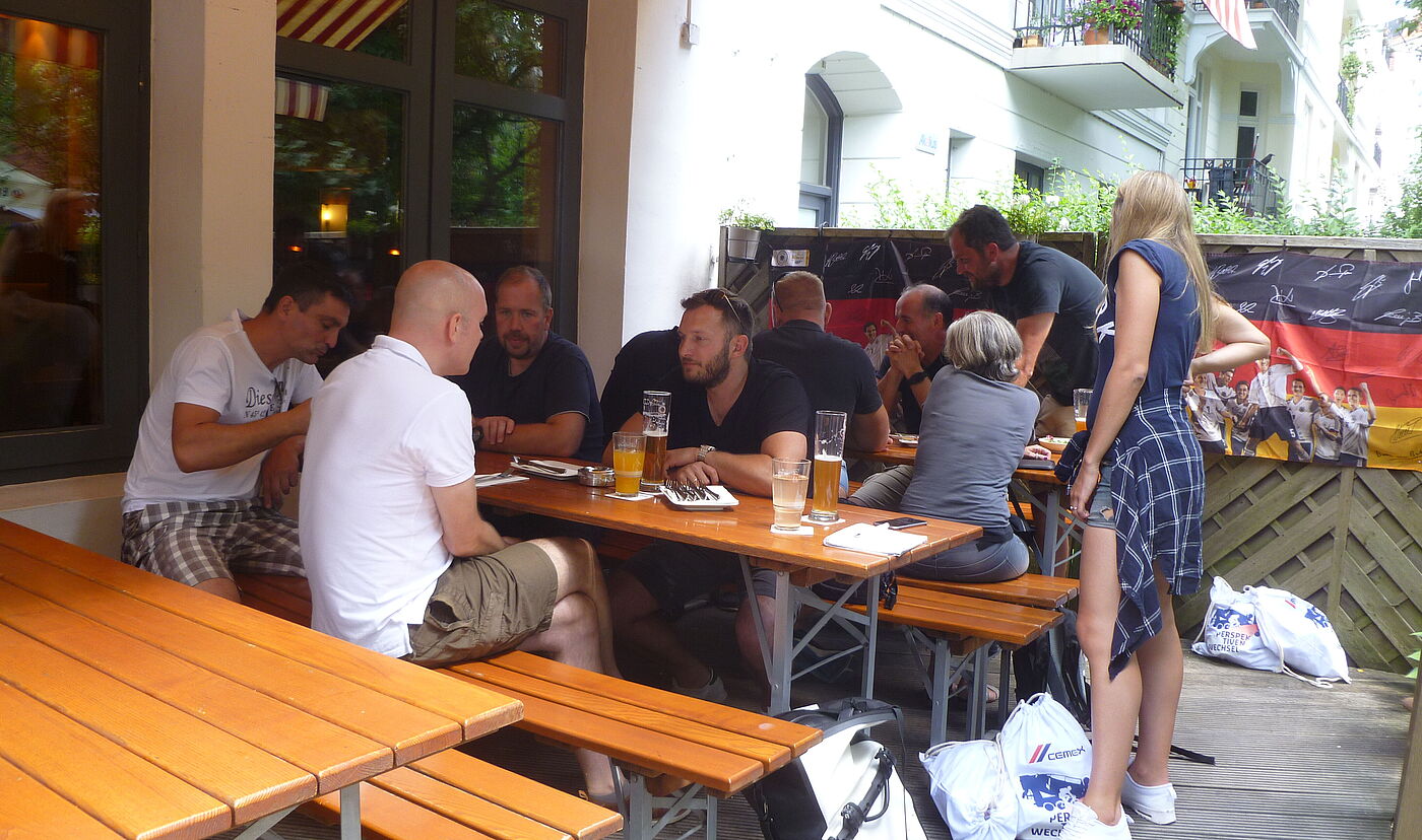 Personen sitzen mit Getränken an Restauranttischen.