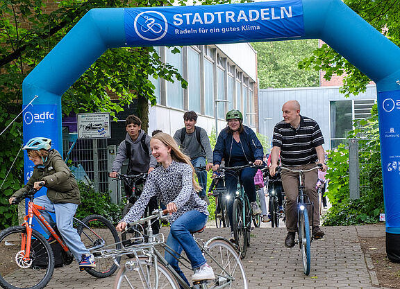 Mehrere Menschen fahren auf Rädern durch ein Tor mit Beschriftung STADTRADELN