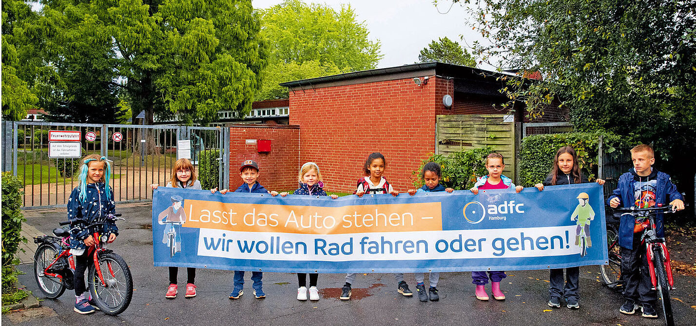 Kinder demonstrieren vor ihrer Schule für weniger Autoverkehr