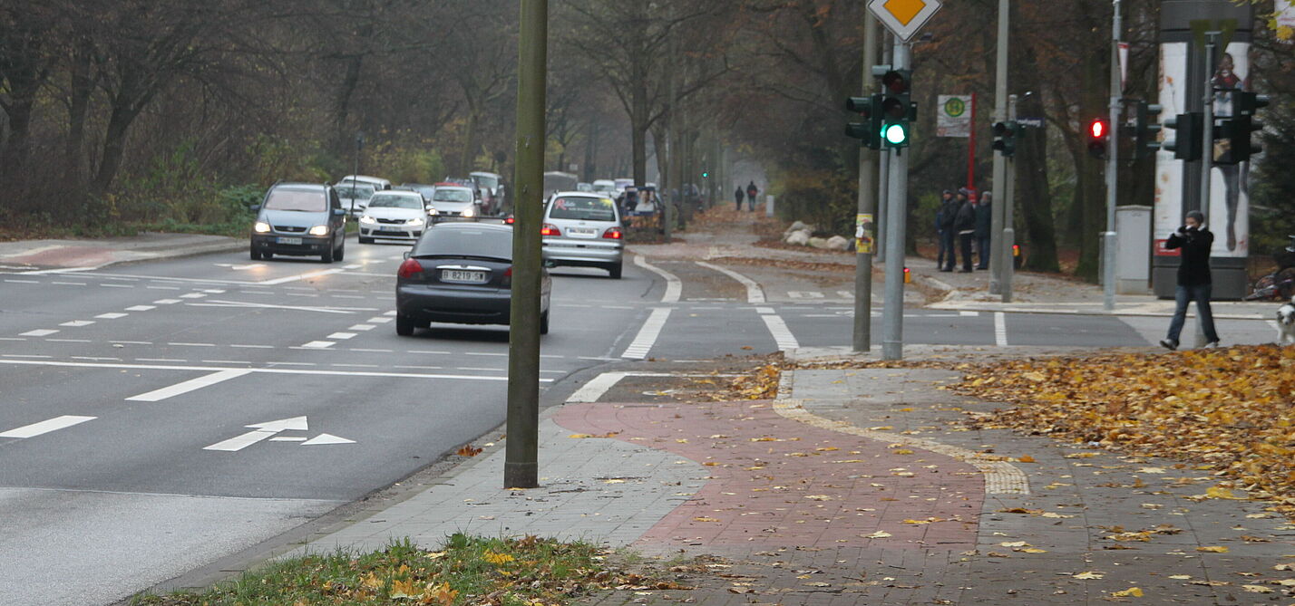 Ein Radweg wird vor der Kreuzung zu einem Radfahrstreifen. Die Fahrbahnampel zeigt grün.