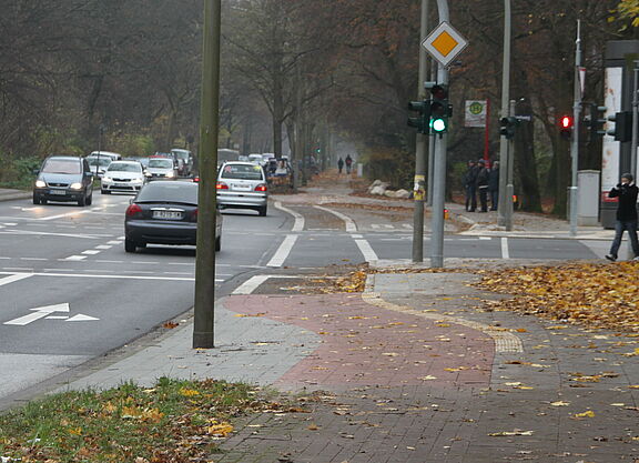 Ein Radweg wird vor der Kreuzung zu einem Radfahrstreifen. Die Fahrbahnampel zeigt grün.