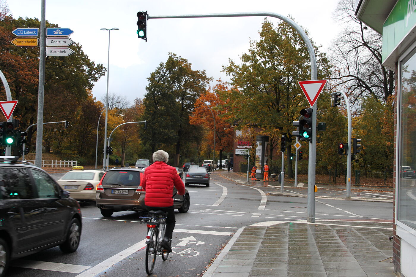 Radfahrerin auf einem Radfahrstreifen auf der Höhe einer grün zeigenden Fahrbahnampel. Im Hintergrund eine weitere Ampel, die aus ist und leicht rechts eine rot zeigene Fußgängerampel