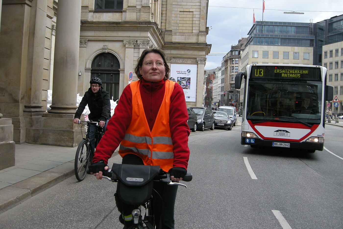 Eine Radfahrerin fährt auf dem rechten Fahrstreifen. Einige Meter hinter ihr folgt ein Bus auf dem linken Fahrstreifen.