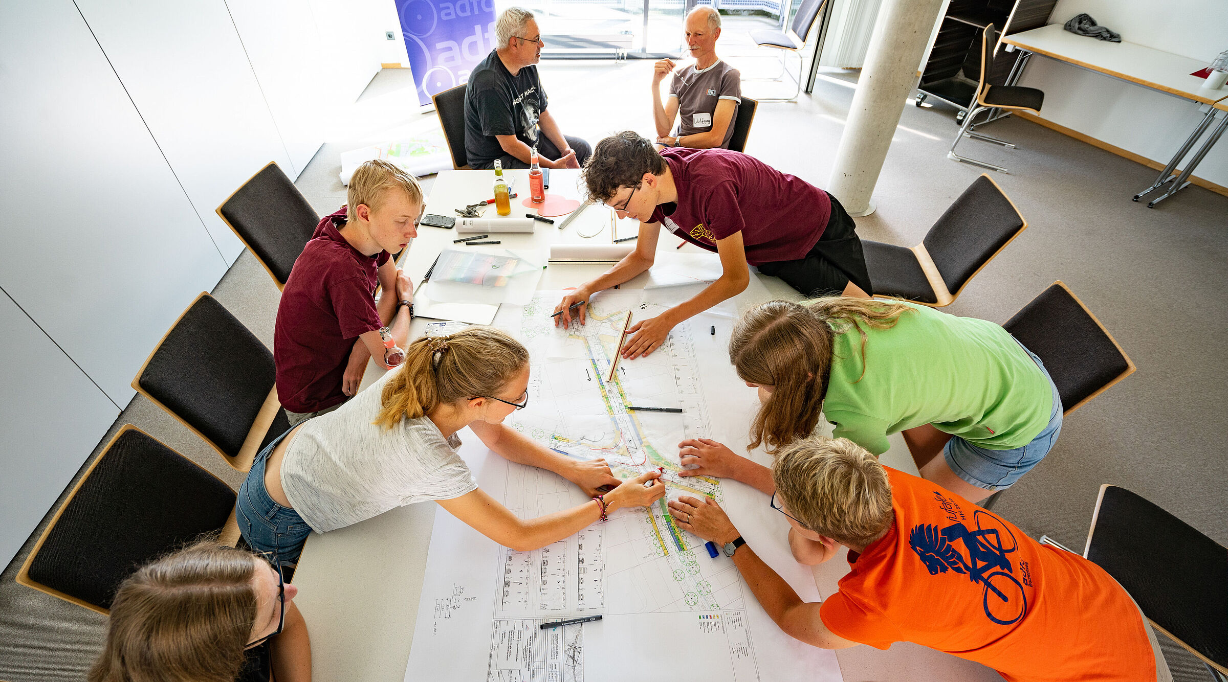 mehrere Personen sind über einem Arbeitstisch gebeugt und bearbeiten gemeinsam Dokumente