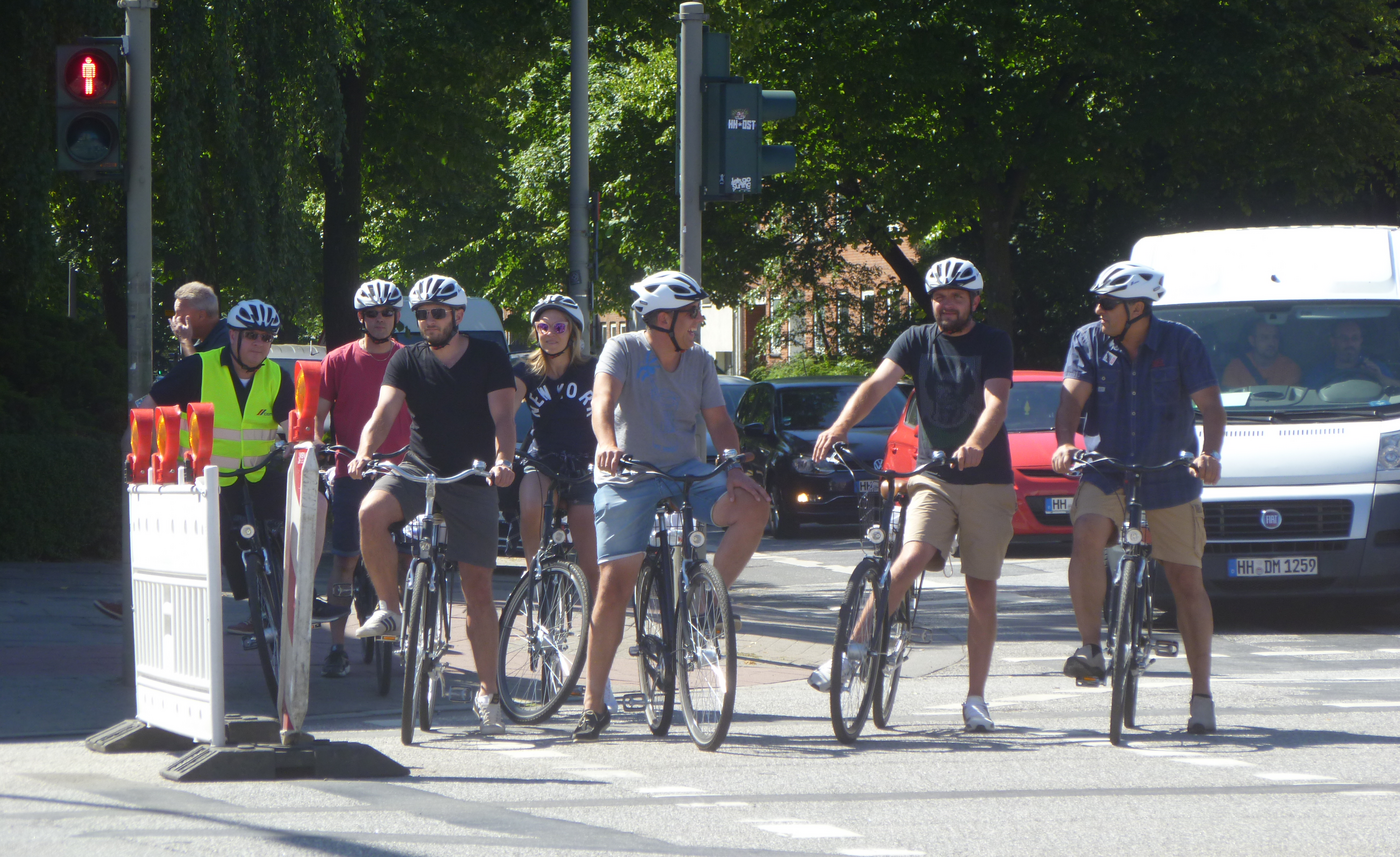 Gruppe von Radfahrenden an einer Ampel stehend.