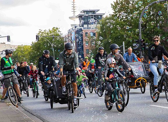 Teilnehmende der Familien-Fahrraddemo Kidical Mass fahren durch einen Seifenblasen-Regen