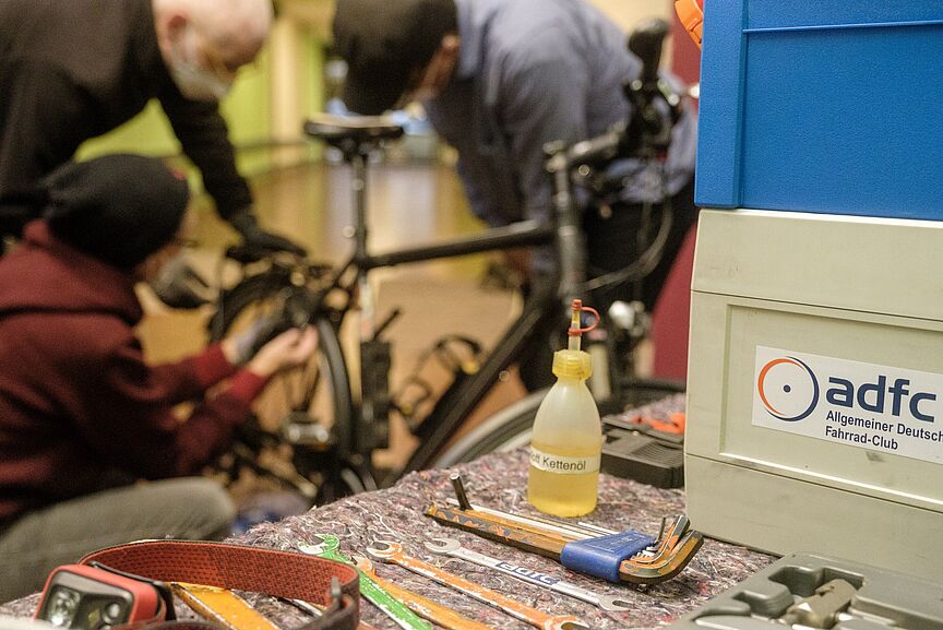 Fahrradreparaturseminar Werkzeuge im Vordergrund, hinten beugen sich Menschen über ein Rad