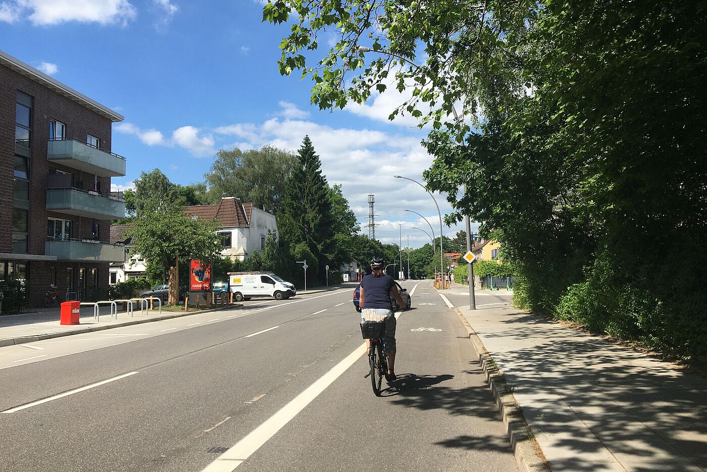 Eine Radfahrerin fährt bei Sonnenschein auf einem Radfahrstreifen. An einer Einmündung auf der Linken Seite steht ein Kleintransporter.