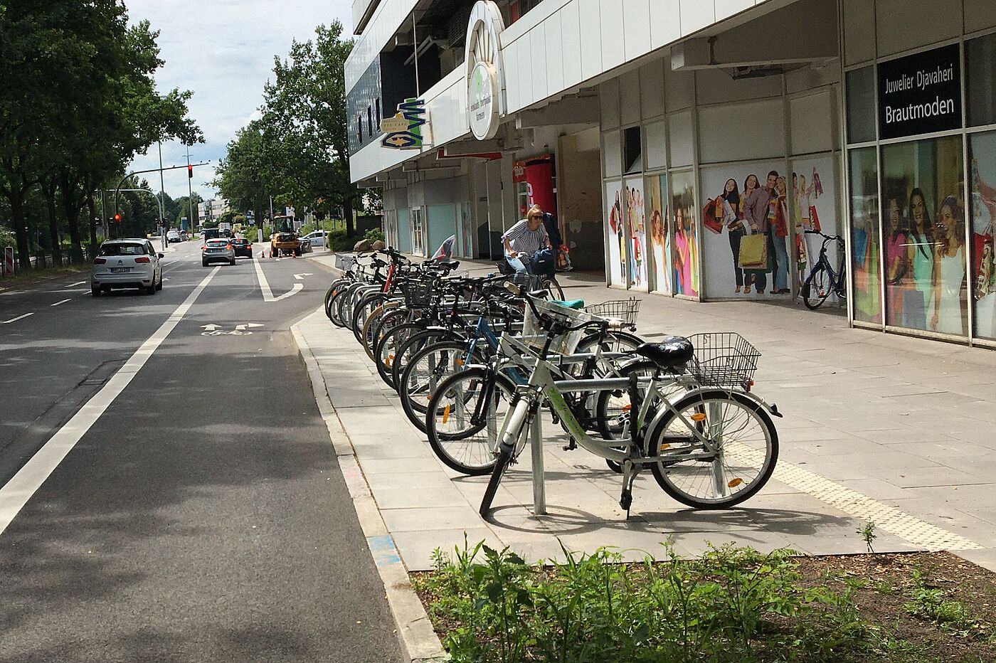 Vor dem Einkaufszentrum Farmsen stehen Fahrräder an Fahrradbügeln. Direkt daneben verläuft der Radfahrstreifen auf dem Friedrich-Ebert-Damm.