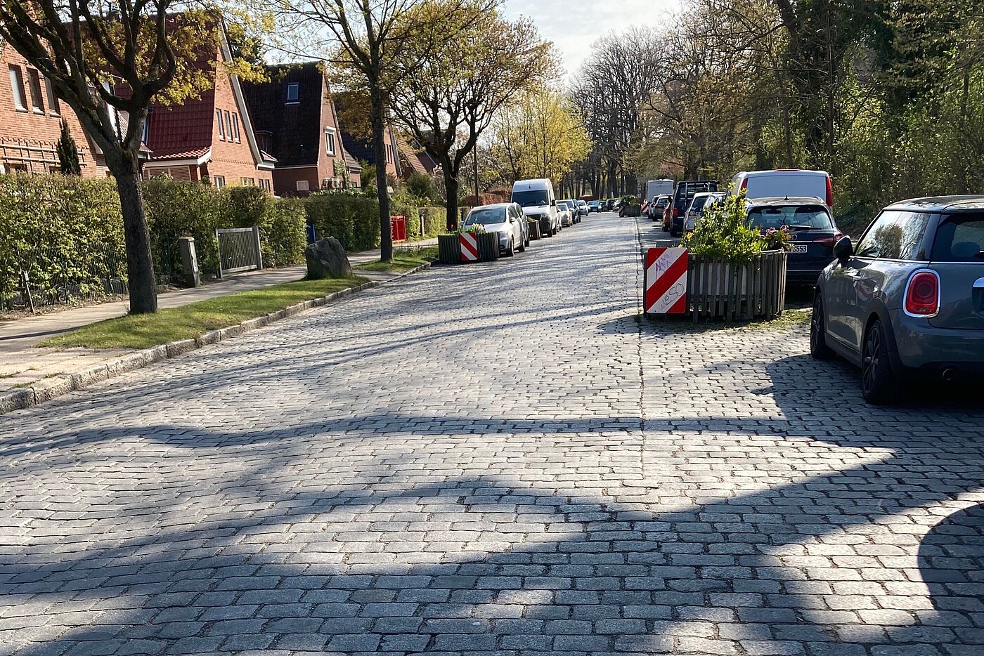 gepflasterte Wohnstraße mit neben und auf der Fahrbahn geparkten Autos