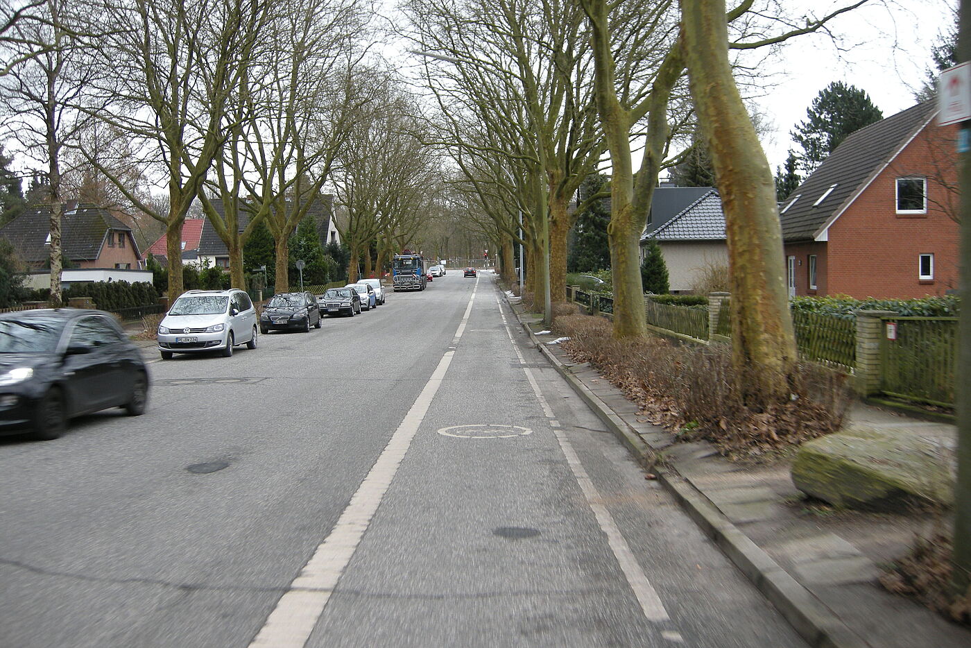 alter Radfahrstreifen auf der einen Seite der Fahrbahn, gegenüber liegt der Radfahrstreifen hinter einer Reihe Falschparker-Autos versteckt