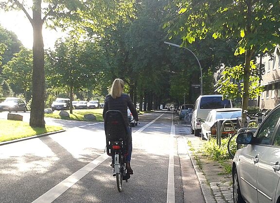 Radfahrerin auf Radfahrstreifen von Bäumen gesäumt