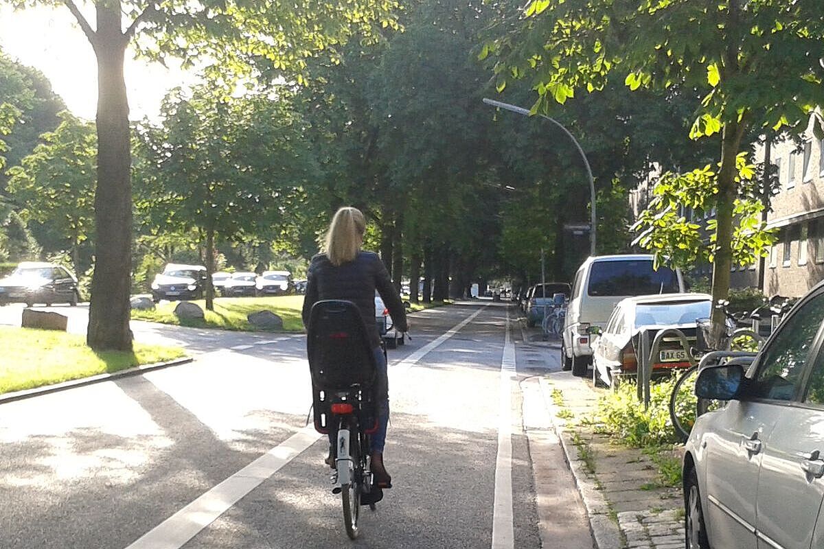 Radfahrerin auf Radfahrstreifen von Bäumen gesäumt