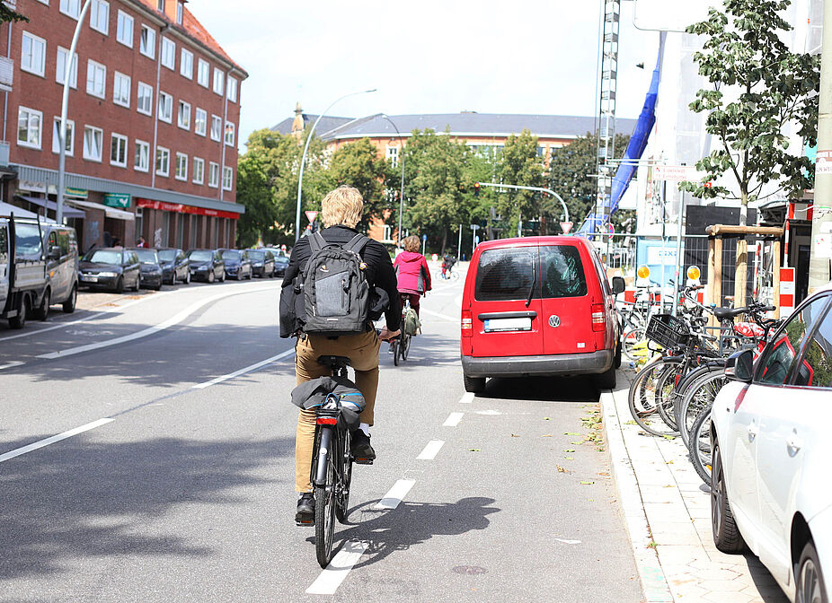 Pressefoto zum Fahrradklimatest: Zugeparkte Radwege, Schutz- und Radfahrstreifen sind für Radfahrende in Hamburg ein großes Problem. Ein PKW parkt auf einem Schutzstreifen, Radfahrende weichen in den fließenden Verkehr aus.